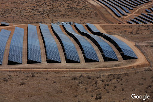 Aerial view of a large solar panel farm on brown arid land, showing rows of photovoltaic panels generating renewable energy.