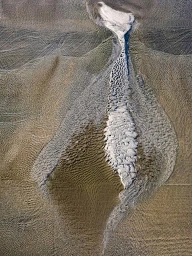 Aerial view of textured sand dunes with winding rivulets of water flowing across the terrain