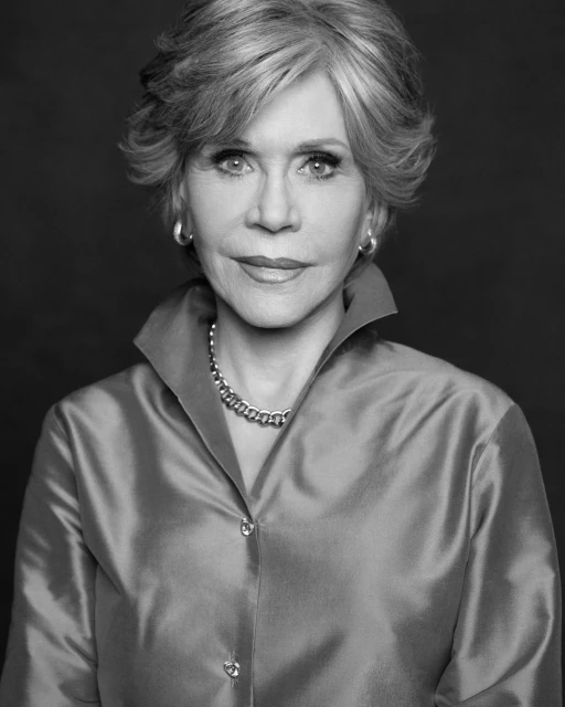 Black and white portrait of an elderly woman with gray hair and a collared satin shirt, posing in front of a dark background.