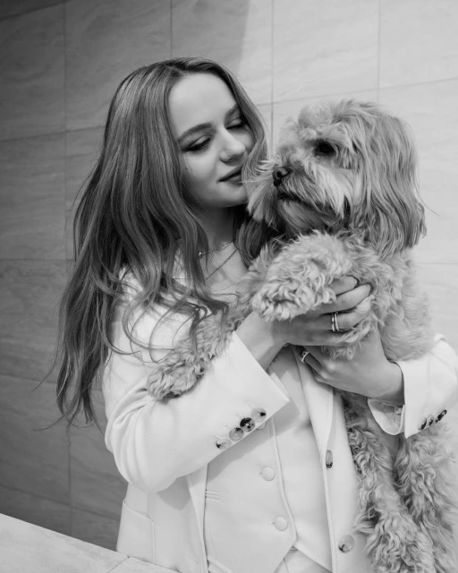 Black and white portrait of a woman in a white suit holding a dog, showcasing a lifestyle fashion editorial.