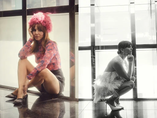Indoor studio shot of a young adult woman wearing a floral long-sleeve top, black skirt, and pink furry hat, posing on a black marble floor.