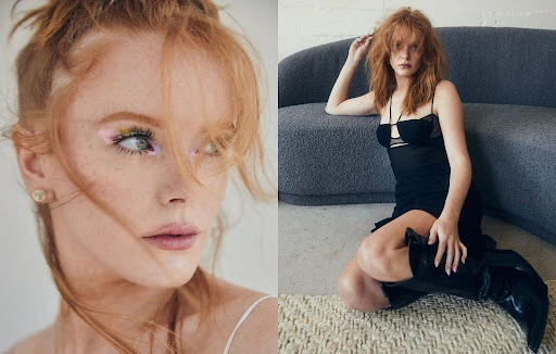 Portrait of a red-haired woman in a black dress and boots, posing on a beige carpet in front of a gray couch in an indoor setting.