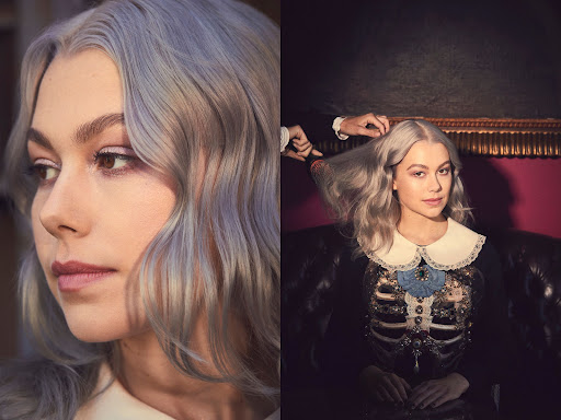 Portrait of musician Phoebe Bridgers with light gray hair in a studio setting, being styled with a hairbrush near a painting.
