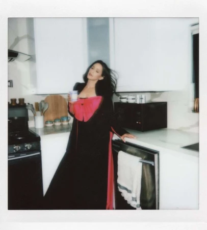 A woman in a black and red robe poses in a modern kitchen with white cabinets, holding a mug in a lifestyle shot. 