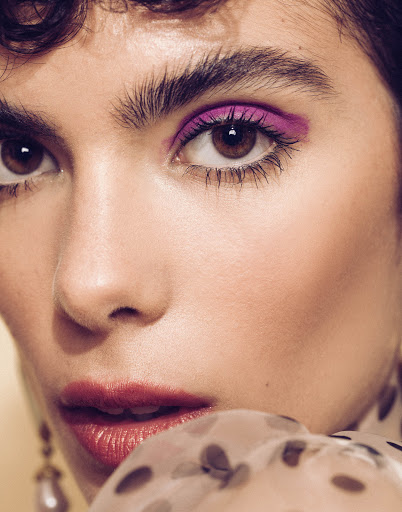 Close-up portrait of a woman with vibrant magenta eyeshadow, dark curly hair, and polka-dot sheer fabric by photographer Sami Drasin.