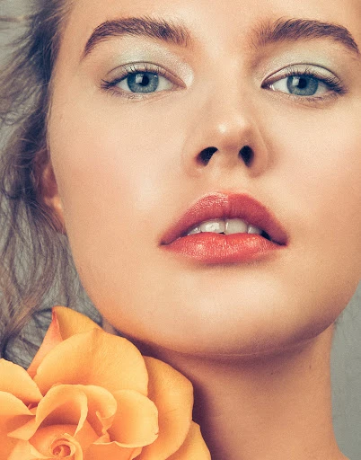 Close-up portrait of a fair-skinned woman with blue eyes and pink lips, alongside a yellow rose, showcasing beauty and skincare.