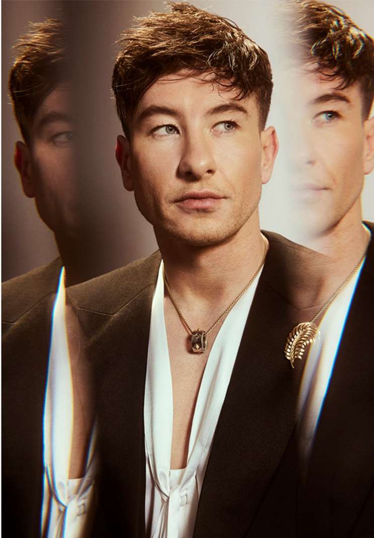 Portrait of a man wearing a black blazer and gold pendant necklace. The image has a blurred effect with two duplicate images behind.