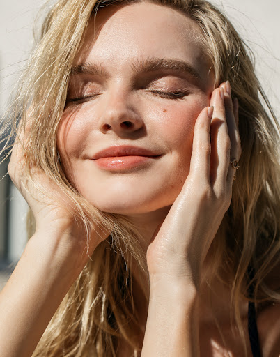 Close up portrait of a blonde woman with eyes closed holding her face with her hands in warm sunlight