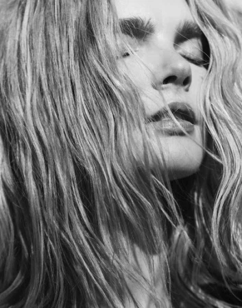 Close-up monochrome portrait of a woman with long tousled hair across her face, shot by Sami Drasin.