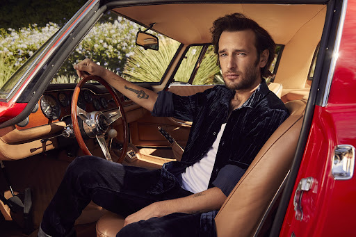 Stylish man in open red convertible car. The man sits in the driver's seat looking at the camera with neutral expression.