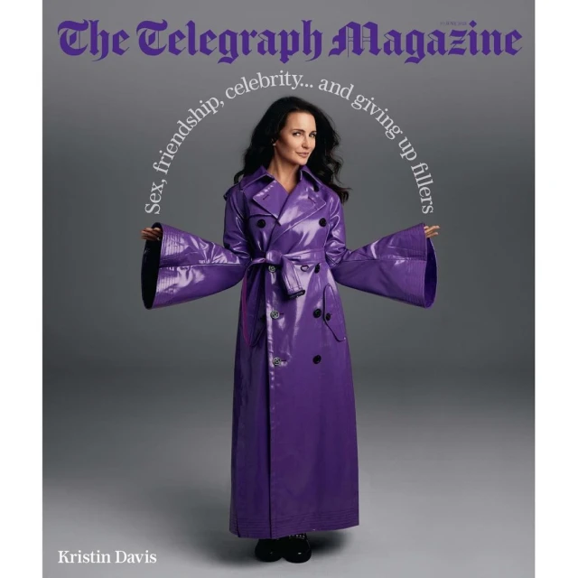 Magazine cover featuring Kristin Davis in a glossy purple trench coat, with headline text and a grey backdrop. Full shot.