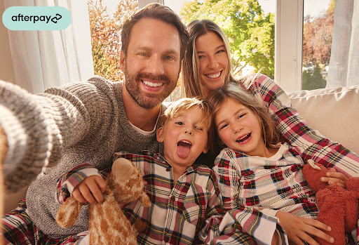 Smiling family of four poses for a selfie indoors, all wearing matching plaid pajamas, creating a cozy and cheerful family portrait.
