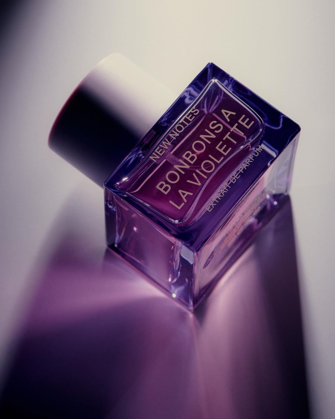 Close-up of a translucent square perfume bottle with a white cap, featuring purple liquid and 'Bonbons a la Violette' text.