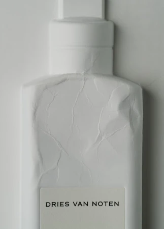 Close-up studio shot of a white Dries Van Noten perfume bottle against a white backdrop with visible paper wrapping texture.