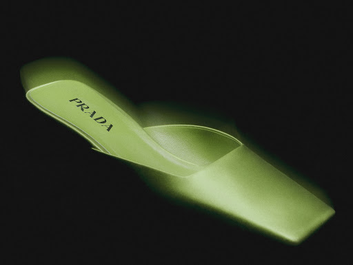Close-up studio shot of a lime-green Prada heeled mule. The shoe has a pointed toe and a glossy, satin-like finish with the Prada logo on the insole.