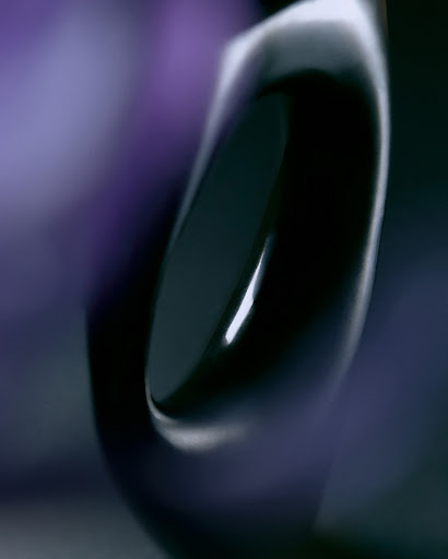 Abstract still life of a glossy dark blue and black object on a blurred backdrop of dark blues and violets.