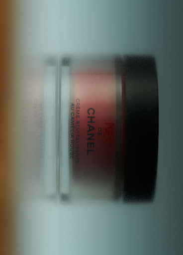 Close-up of a Chanel cream jar in a clear container with a black lid. The label is visible, showcasing brand text.