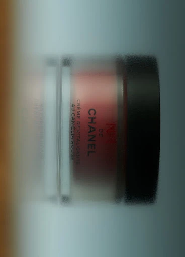 Close-up of a Chanel cream jar in a clear container with a black lid. The label is visible, showcasing brand text.