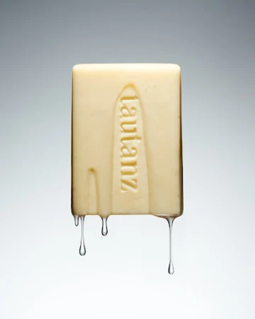 Close-up of a rectangular bar of soap with the word 'lautanz' vertically embossed, set against a smooth, graduated grey background.