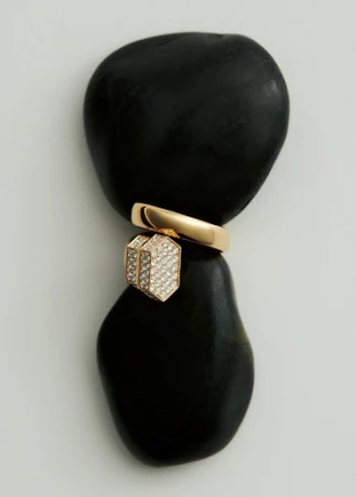 Still life of a gold ring and pendant jewelry piece balancing on two smooth black stones against a light neutral background.