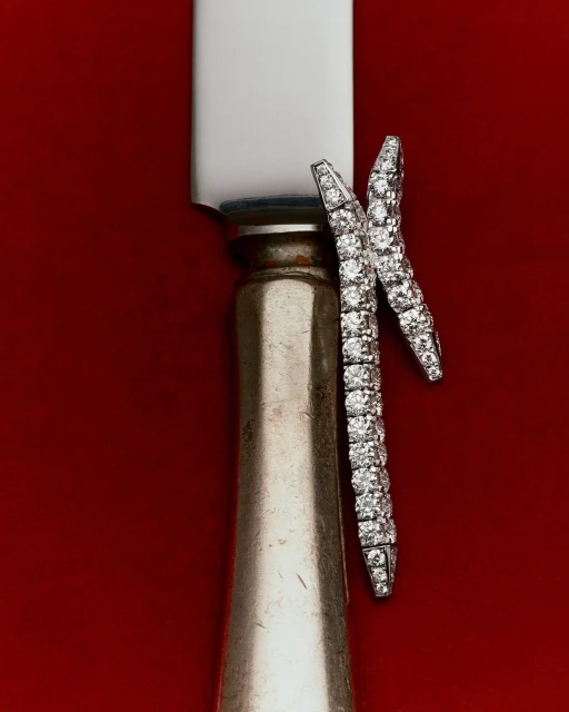 Close-up studio shot of a vintage silver knife with diamond bracelets draped on the handle, set against a rich, solid red background.