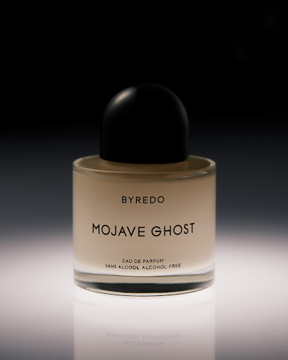 Close-up product shot of a Byredo Mojave Ghost perfume bottle on a reflective white surface against a dark background. Elegant and simple.