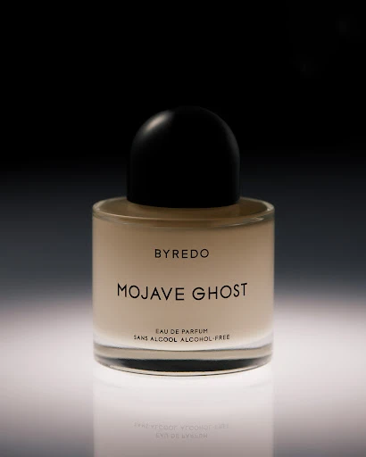 Close-up product shot of a Byredo Mojave Ghost perfume bottle on a reflective white surface against a dark background. Elegant and simple.