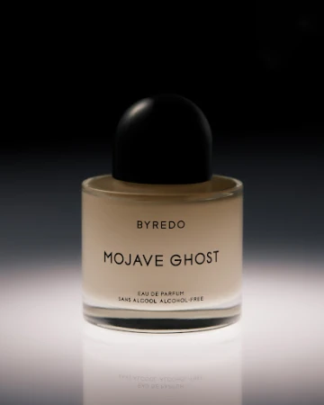 Close-up product shot of a Byredo Mojave Ghost perfume bottle on a reflective white surface against a dark background. Elegant and simple.