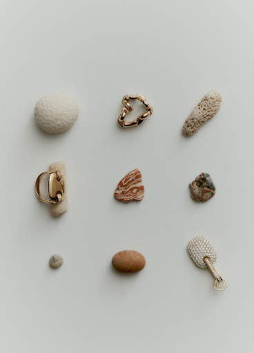 High-angle studio shot of scattered jewelry pieces, stones, and coral on a white background with neutral, muted color palette.