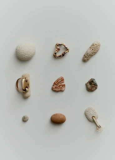High-angle studio shot of scattered jewelry pieces, stones, and coral on a white background with neutral, muted color palette.