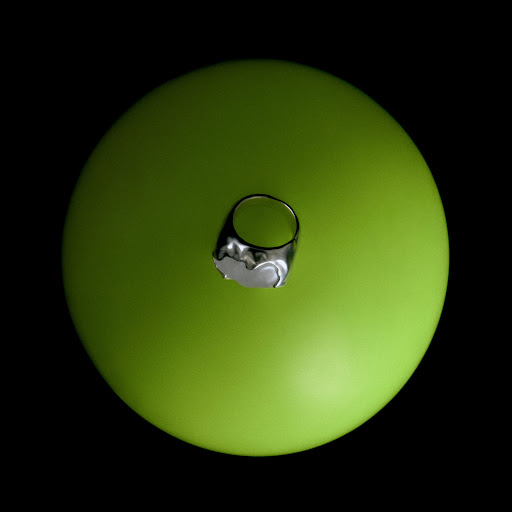 Overhead studio shot of a silver ring with a white stone on a green sphere against a black background, jewellery and product photography.