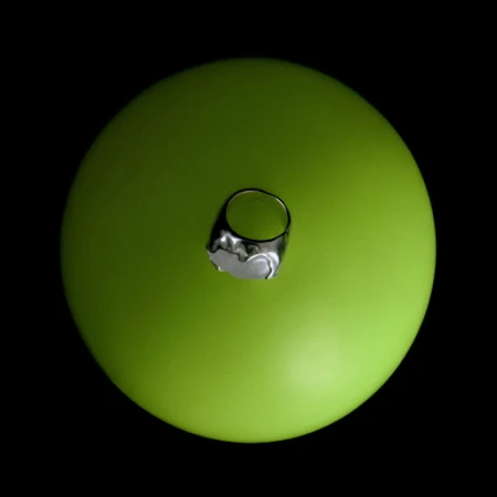Overhead studio shot of a silver ring with a white stone on a green sphere against a black background, jewellery and product photography.