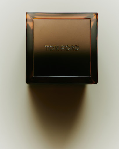 Close-up of a square-shaped Tom Ford perfume bottle with a brown gradient on a cream surface, showcasing luxury beauty product.