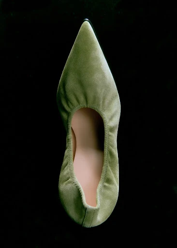 Overhead shot of a green velvet women's pointed-toe flat on a black background, showcasing its design and material.
