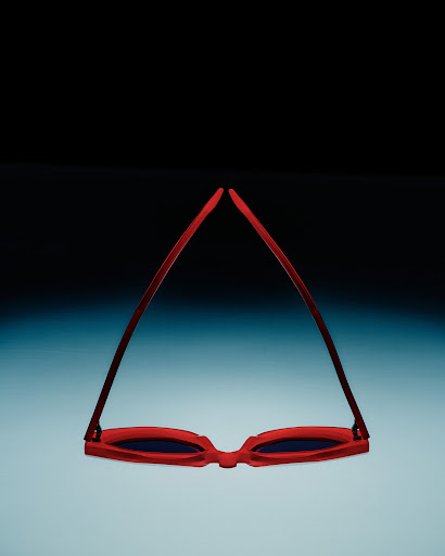 Red framed sunglasses isolated against a gradient blue and black background, lying upside down with the lenses facing the viewer.