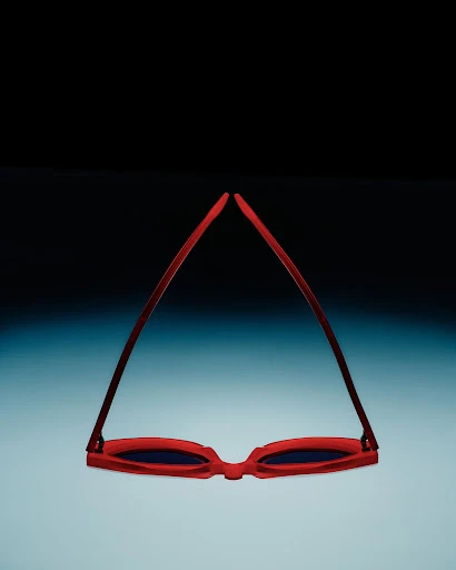 Red framed sunglasses isolated against a gradient blue and black background, lying upside down with the lenses facing the viewer.