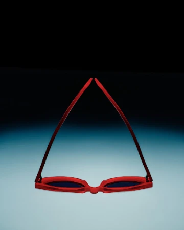 Red framed sunglasses isolated against a gradient blue and black background, lying upside down with the lenses facing the viewer.