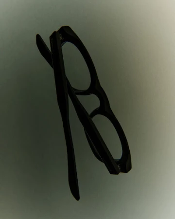 Black eyeglasses with a classic frame design are angled slightly on a neutral gray background.