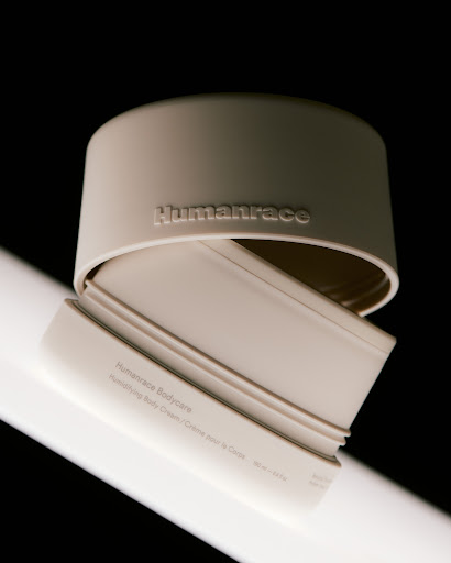 Beige Humanrace Bodycare container with lid on a gradient black backdrop, studio lit, showcasing skincare product.