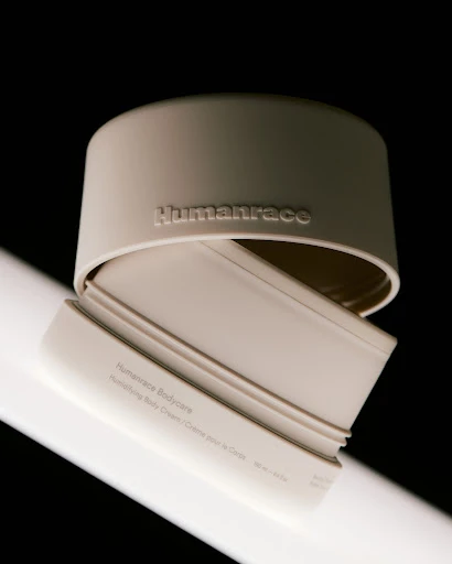 Beige Humanrace Bodycare container with lid on a gradient black backdrop, studio lit, showcasing skincare product.