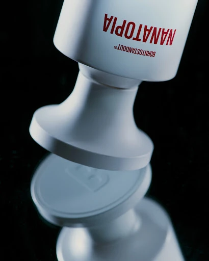 Close-up studio shot of a glossy white bottle with red sans-serif text on a reflective black surface, emphasizing product design.