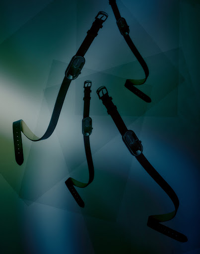 Abstract product shot of several wristwatches with black leather bands floating in a dark blue and green diffused studio environment.