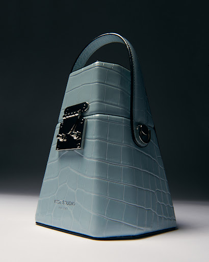Light blue Yuzefi handbag featuring a mock crocodile texture, top handle, and silver hardware.  Studio product shot with gradient background.