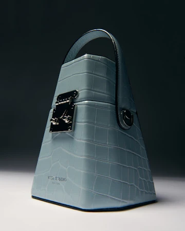 Light blue Yuzefi handbag featuring a mock crocodile texture, top handle, and silver hardware.  Studio product shot with gradient background.