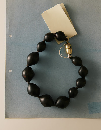 Necklace made of black beads with a gold clasp is displayed on a blue surface with paper tags, jewelry fashion photography.