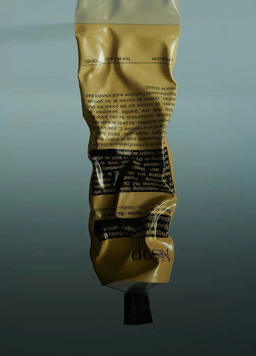 A golden-yellow Aesop Reverence Aromatique Hand Balm tube against a grey gradient background in a studio product shot.