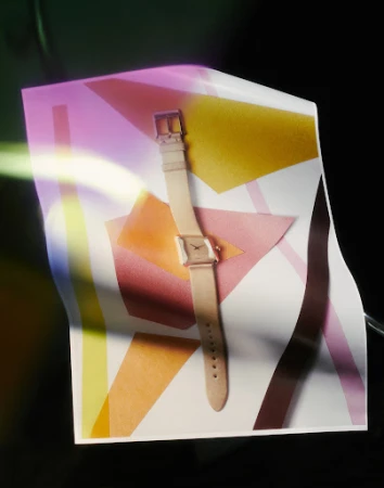 Elegant wrist watch with a neutral band and square face on a geometric white and pastel patterned surface in a studio setting.