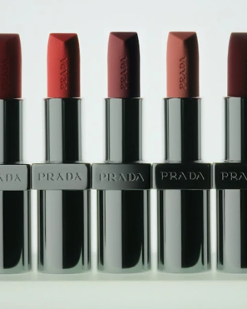 Five Prada lipsticks in silver metallic cases arranged in a neat row against a bright white background.