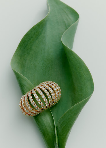 A diamond pave ring rests on a curved green leaf against a minimal white background by Sara Zanoni