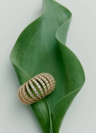 A diamond pave ring rests on a curved green leaf against a minimal white background by Sara Zanoni